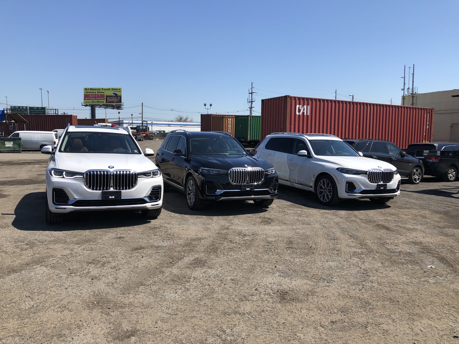 Three premium SUVs staged in front of shipping containers at an export yard, ready for worldwide delivery.